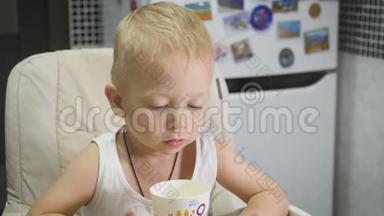 可爱的小男孩在家吃早餐时喝牛奶，同时在平板电脑上看卡通。 儿童和技术